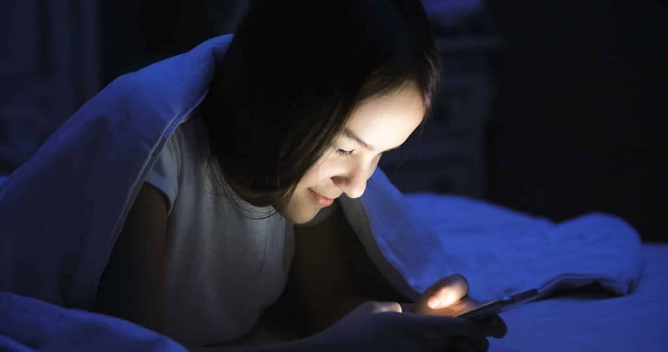 Jugendliche mit Smartphone im Bett