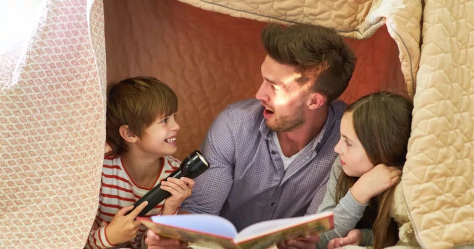Vater und Kinder mit Taschenlampe beim vorlesen