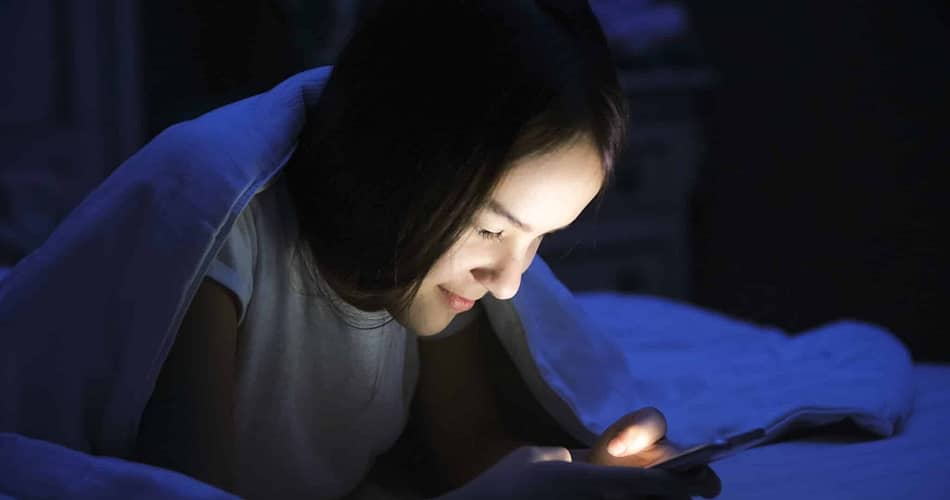 Jugendliche mit Smartphone im Bett